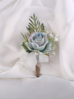 Ombre blue rose boutonniere with green foliage, white ribbon and a small pearl