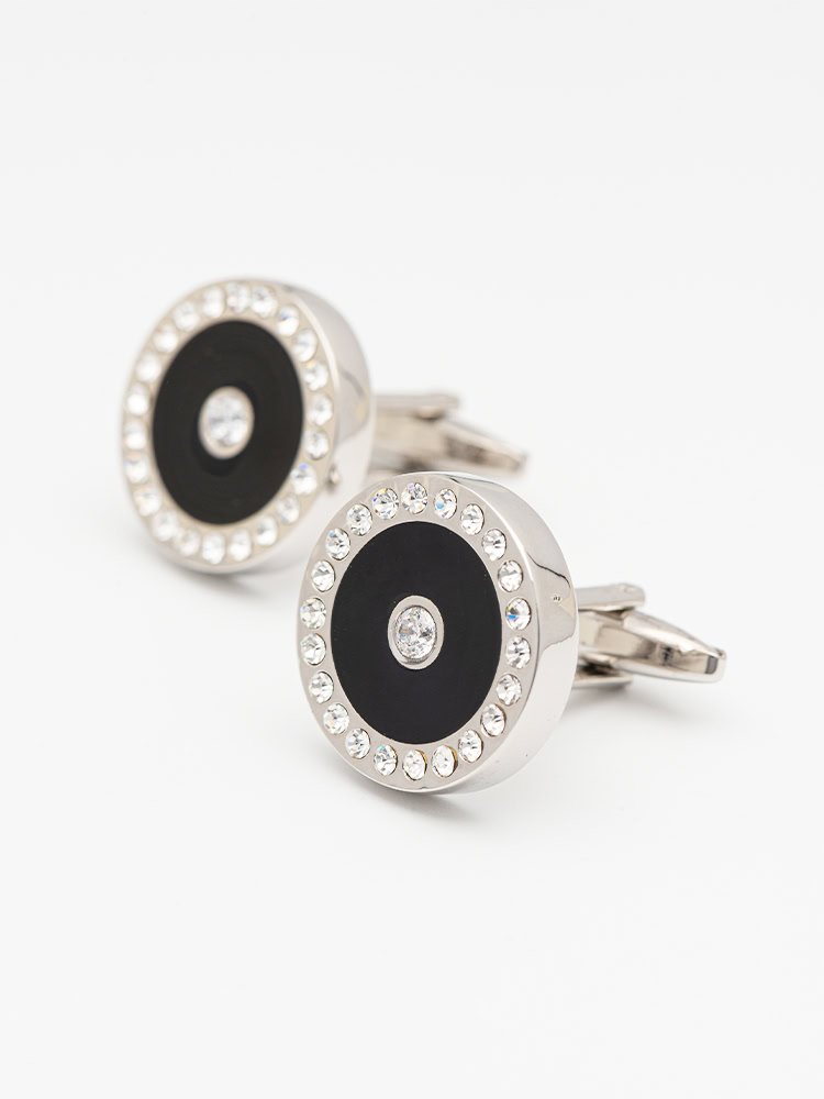A pair of circular black - and - silver cufflinks with sparkling crystals.