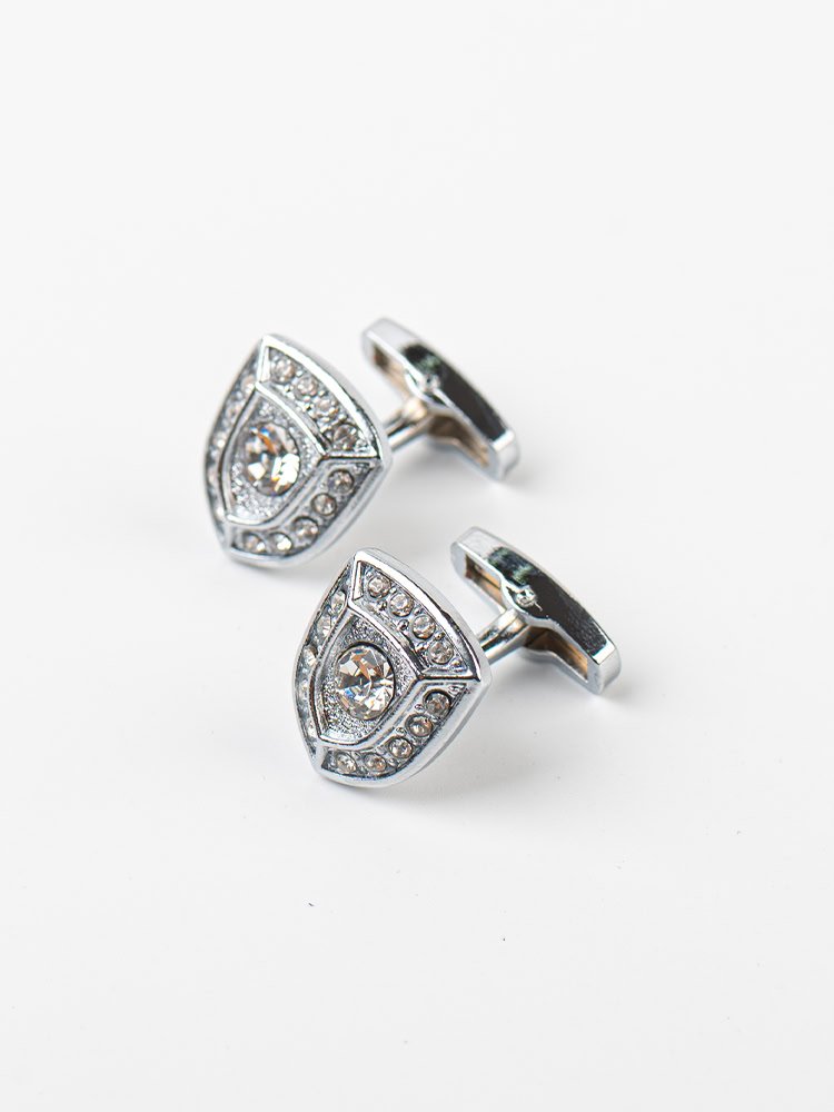 A pair of shield - shaped silver cufflinks adorned with sparkling crystals.