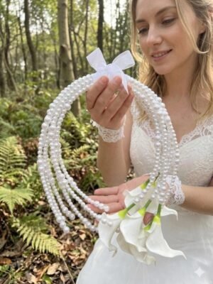 Bride styling a white calla lily pearl hoop bouquet in an outdoor wedding setting